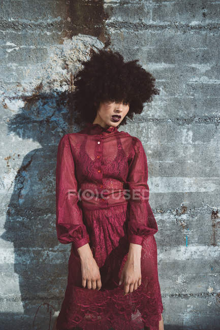 Portrait of curly brunette girl with afro posing in red dress over concrete wall — Stock Photo