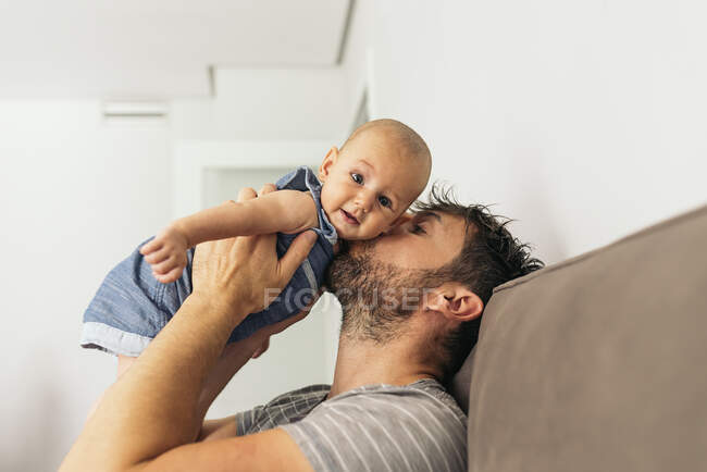 Seitenansicht des bärtigen Vaters, der sein süßes Baby küsst und in die Kamera schaut — Stockfoto