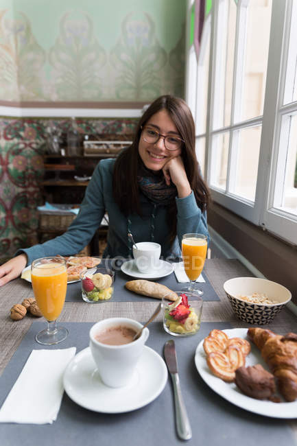 Portrait of brunette girl leaning with cheek on fist and looking at camera at breakfast table — Stock Photo