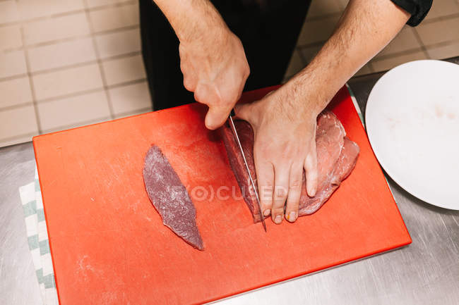 Acima da vista da cultura de mãos masculinas cortando carne a bordo na cozinha do restaurante — Fotografia de Stock