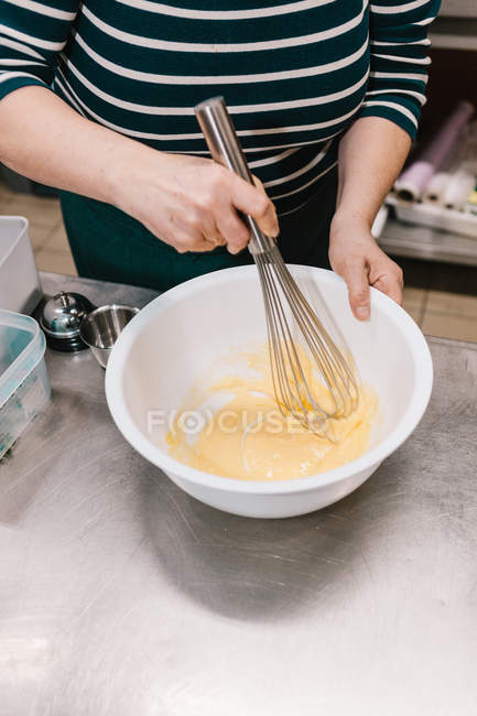 Imagen recortada de hembra golpeando ingredientes con batidor en la mesa en la cocina del restaurante - foto de stock