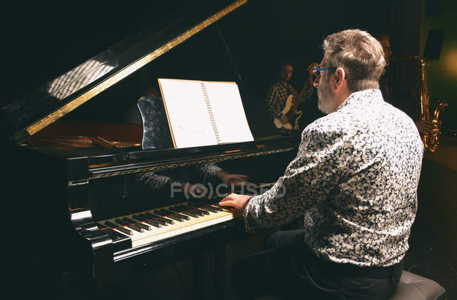 Rückansicht eines Mannes, der im Hintergrund Klavier spielt, mit Menschen, die andere Instrumente spielen — Stockfoto