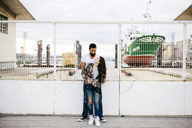 Couple posing near industrial wharf fence — Stock Photo