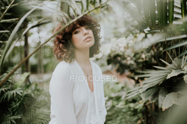 Sensual brunette girl posing at greenery and looking at camera — Stock Photo