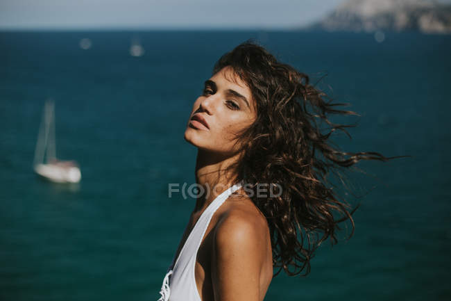 Портрет брюнетки с ветреными волосами, позирующей над морским пейзажем с плавающими яхтами — стоковое фото