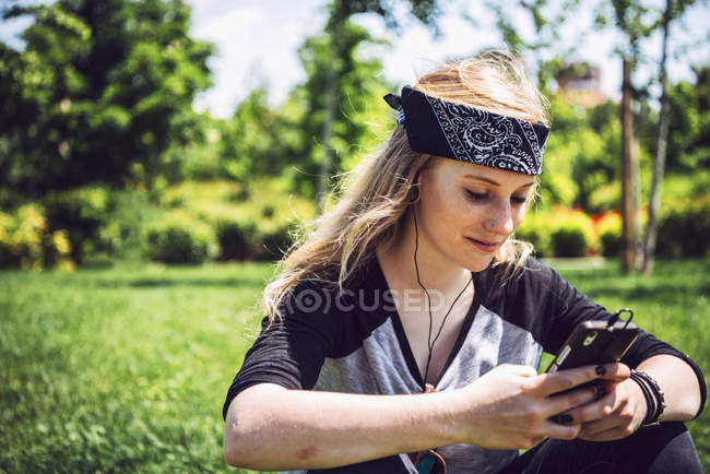 Mujer skateboarder escuchando música desde un smartphone en el parque - foto de stock