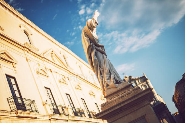 Вид на низький кут кам'яної статуї на фоні орнаментальних фасадів — стокове фото