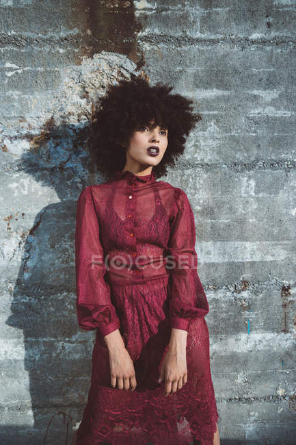 Portrait of curly brunette girl with afro posing in red dress over concrete wall — Stock Photo