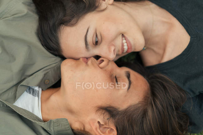 Top view of boy lying face to face with girlfriend and kissing in forehead — Stock Photo