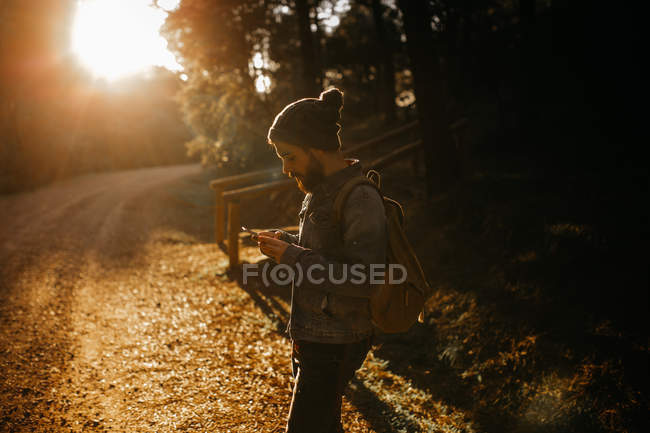Человек просматривает мобильный телефон на лесной дороге — стоковое фото