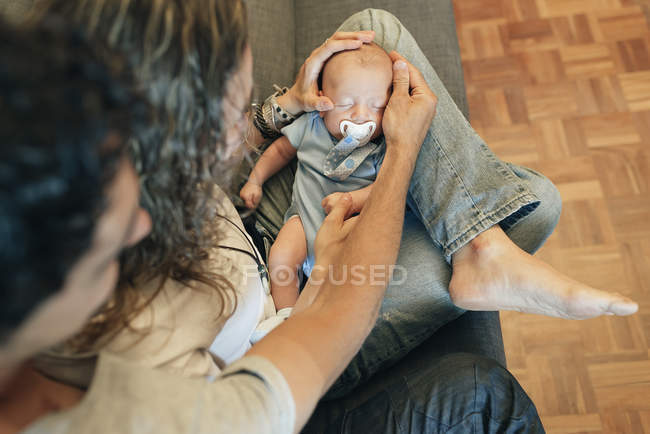 Young couple holding sleeping newborn baby on knees and admiring — Stock Photo