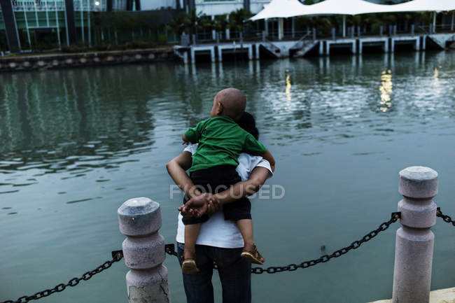 Malaysia - 23. April 2016: Rückansicht eines Mannes, der ein Kind huckepack auf dem Hintergrund des Flusses gibt. — Stockfoto