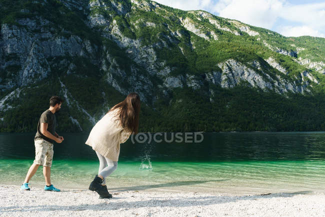 Pareja lanzando piedras al lago de montaña - foto de stock