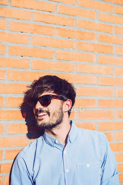 Hombre joven en gafas de sol posando contra la pared de ladrillo - foto de stock