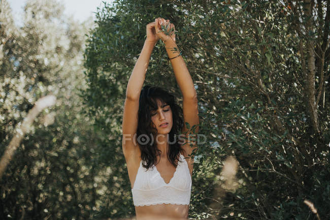 Portrait of brunette woman with eyes closed stretching arms up among green trees — Stock Photo