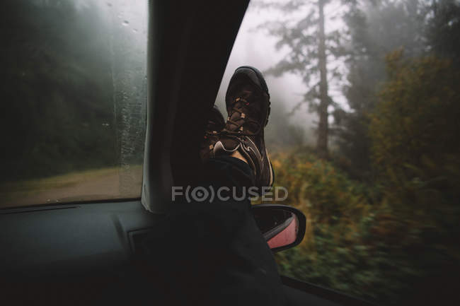 Las piernas de la persona que pone fuera de la ventana del coche en el bosque . - foto de stock