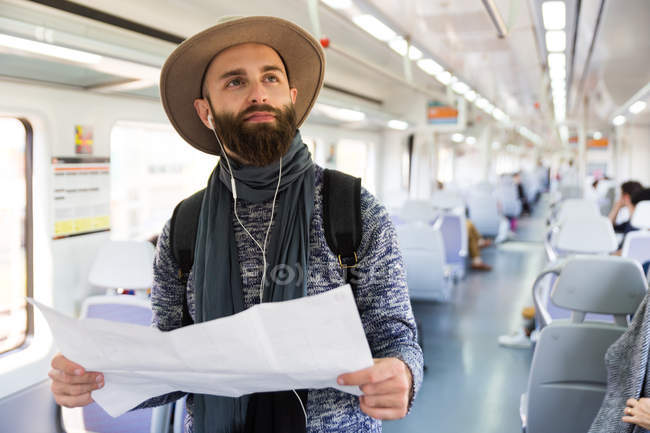 Retrato de homem barbudo com mapa ouvindo música em vagão de trem — Fotografia de Stock