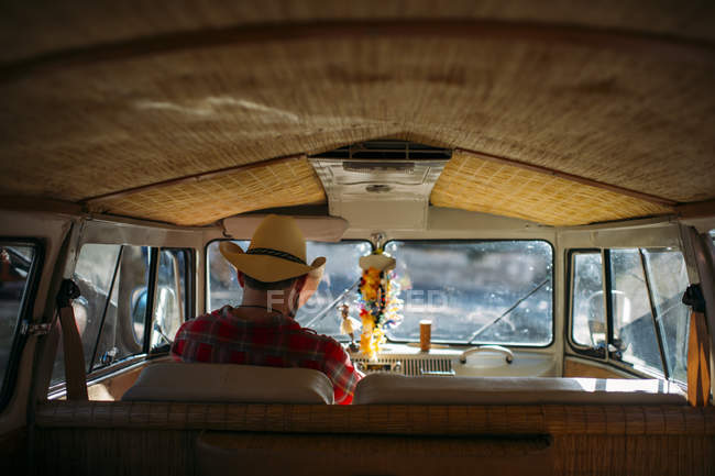 Visão traseira do homem de chapéu de cowboy sentado no assento de motoristas de van retro — Fotografia de Stock