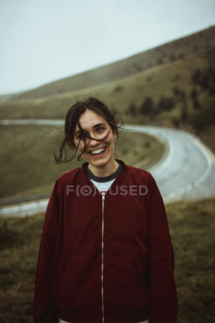 Mujer sonriente con el pelo desordenado en el camino de asfalto en el campo . - foto de stock