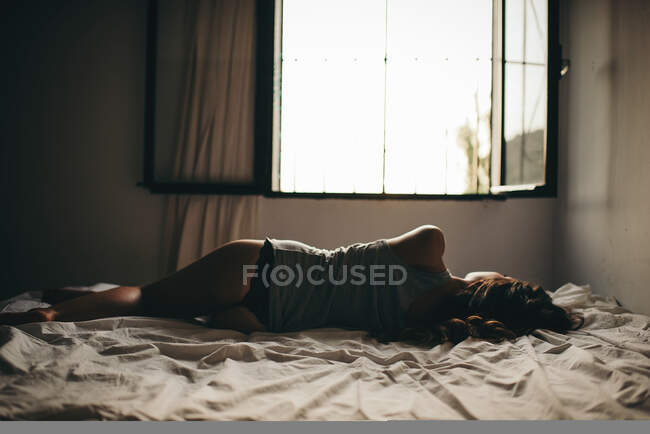 Visão traseira do modelo magro na tanga deitada na cama contra a janela aberta — Fotografia de Stock