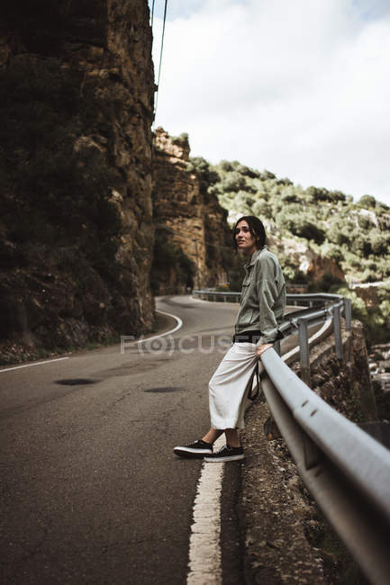 Jeune femme penchée sur la clôture au bord de la route dans les montagnes . — Photo de stock