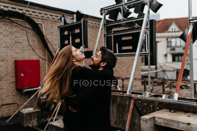 Happy couple in outfit hugging each other on rooftop. — Stock Photo