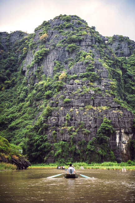 Rear view of man oaring boat tropical river by huge cliffs — Stock Photo
