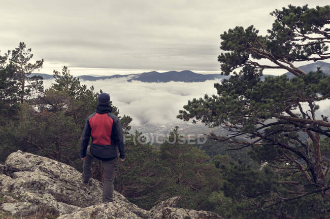El hombre en la cima de la montaña mira las nubes a sus pies en un frío otoño da - foto de stock