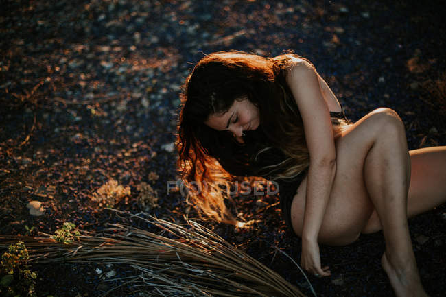 Cheerful young girl in shorts posing on ground in sunset light — Stock Photo