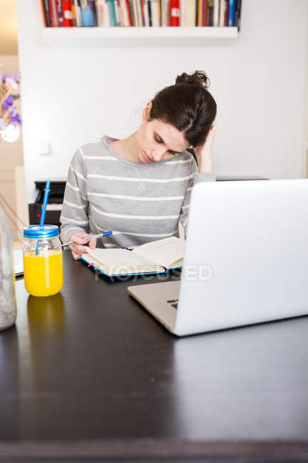 Брюнетка дівчина сидить за столом з ноутбук та jar апельсинового соку і дивлячись на ноутбук — стокове фото