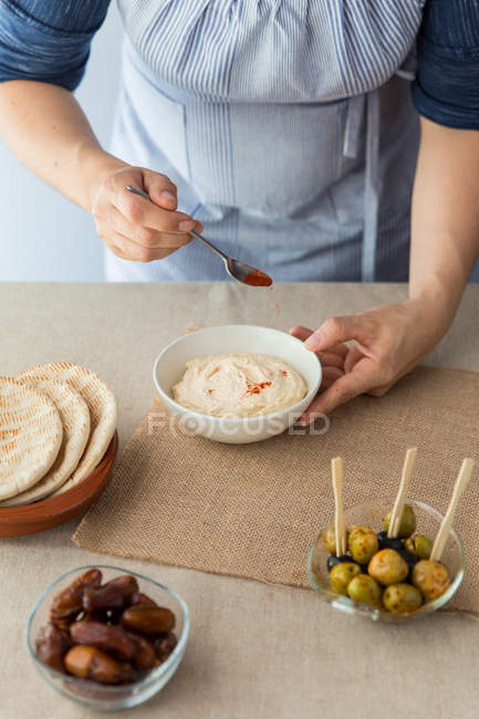Woman decorating hummus with paprika — Stock Photo