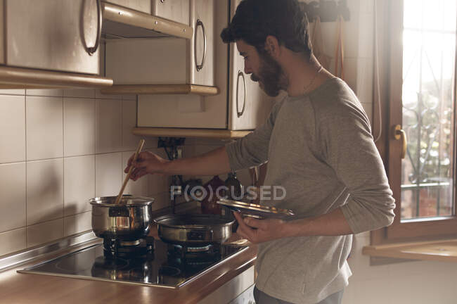 Homem comum cozinhar banhado na luz suave que vem através da janela — Fotografia de Stock