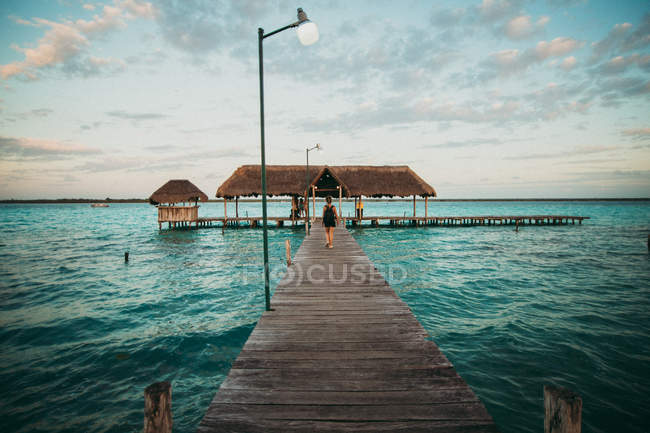 Vista trasera del hombre caminando sobre el muelle de madera en el agua turquesa del océano . - foto de stock