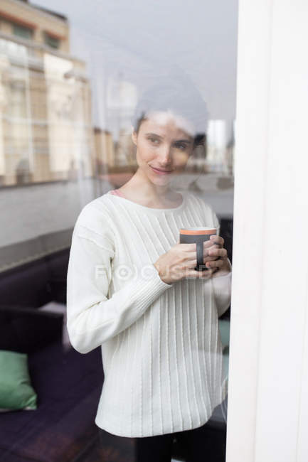 Portrait of brunette girl posing with cup of cocoa behind glass — Stock Photo