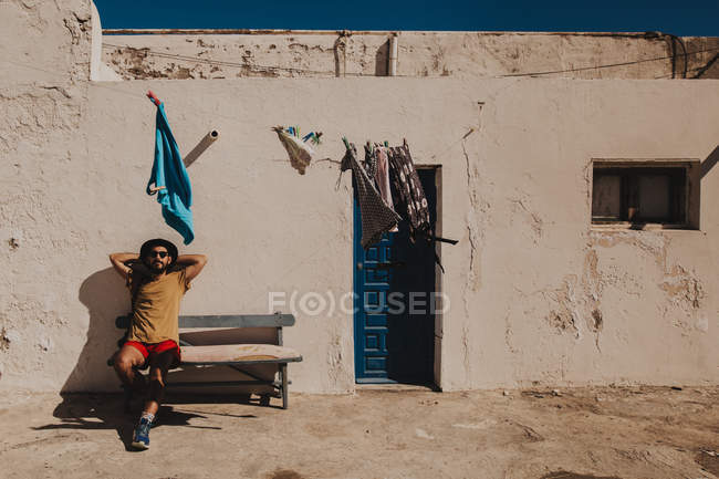 Seduta turistica su panca con braccia sulla testa accanto edificio casa rurale — Foto stock