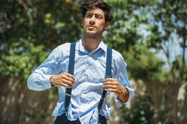 Portrait of good-looking stylish man with hands on suspenders walking in sunlight.Bokeh — Stock Photo