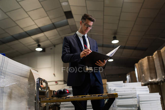 Seriöser Mann steht in Fabrikhalle am Tisch und liest Dokumente durch. — Stockfoto