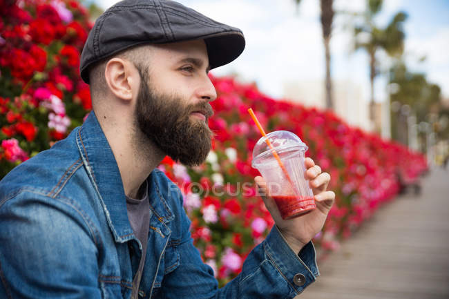 Portrait of man sitting at street and drinking fresh smoothie — Stock Photo