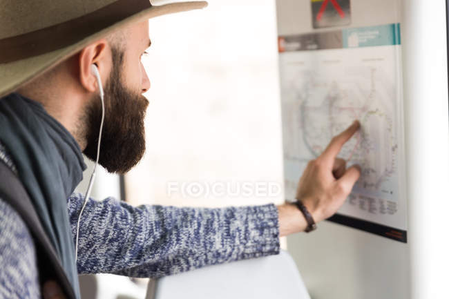 Man in earphones pointing with finger on station map. — Stock Photo