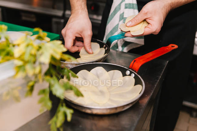 Крупним планом чоловічі руки розміщують скибочки картоплі на сковороді за столом ресторану — стокове фото