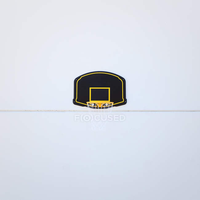 Llanta de baloncesto amarilla sobre tablero negro y amarillo sobre pared blanca - foto de stock