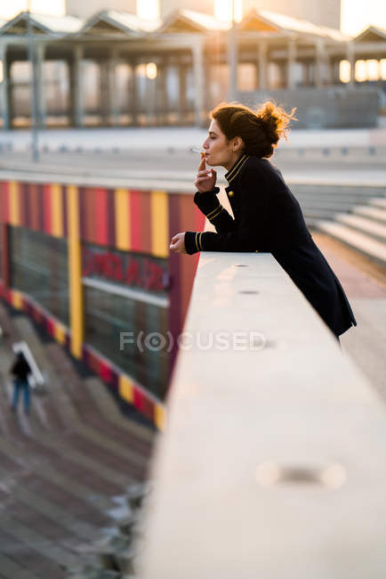 Jeune femme debout à la main courante et fumer — Photo de stock