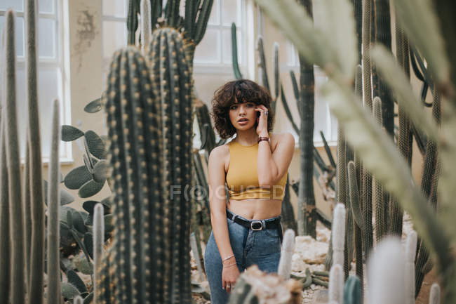 Чуттєва брюнетка дівчина в жовтому верхньому позує серед кактусів — стокове фото