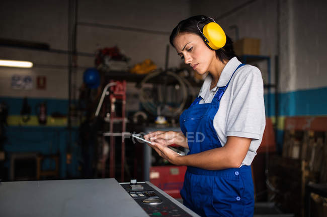 Female mechanic wearing protective headphones using tablet computer in garage — Stock Photo
