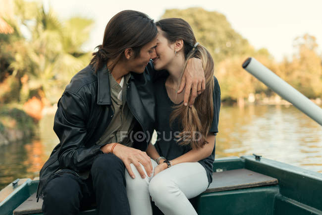 Portrait of young couple kissing and embracing in boat at lake. — Stock Photo