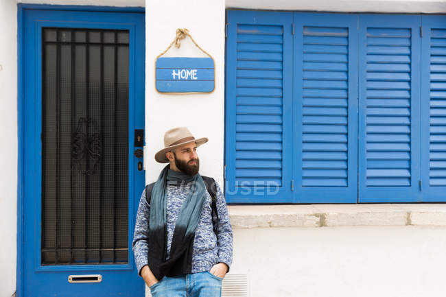 Homme barbu dans le chapeau appuyé sur la façade sous la plaque avec le mot à la maison . — Photo de stock