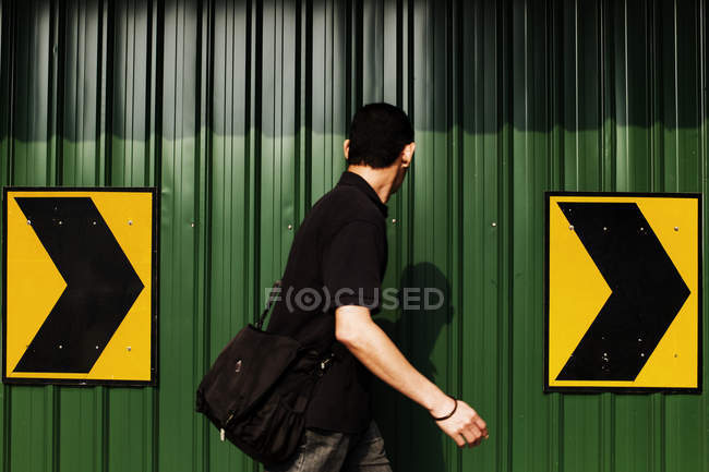 Malaysia- mart 31, 2016: Seitenansicht eines Mannes, der auf dem Hintergrund eines grünen Metallzauns mit Richtungspfeilen geht. — Stockfoto