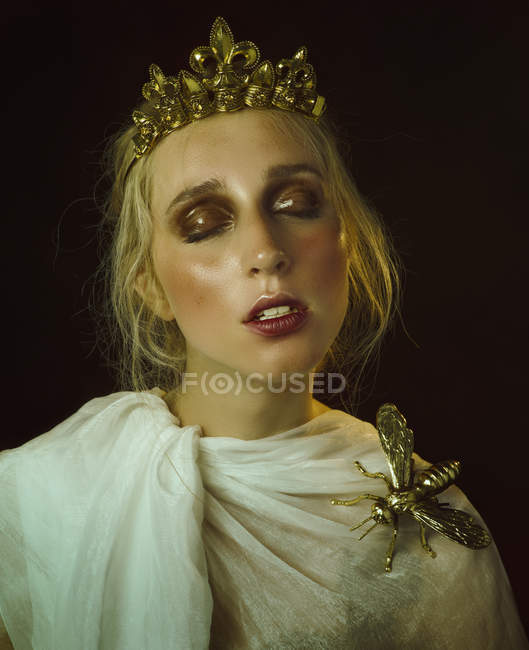 Woman with diadem and dragonfly figurine on shoulder wearing historical dress with eyes closed. — Stock Photo
