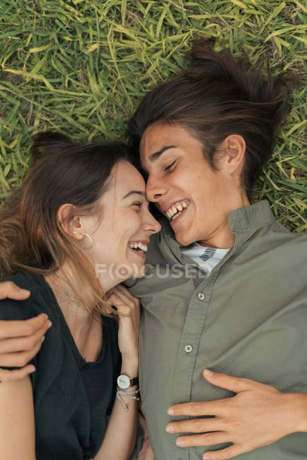 Top view of laughing embracing couple lying on grass and looking at each one — Stock Photo
