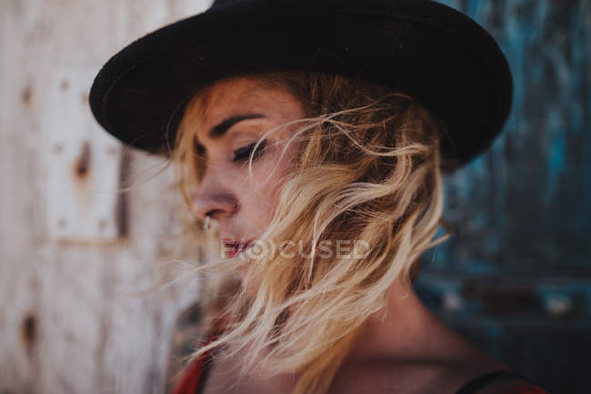 Mujer rubia romántica en sombrero con tabique y cabello ventoso mirando hacia abajo - foto de stock